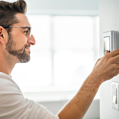 A man programming his thermostat and smiling because he received excellent service from our residential HVAC contractor in London, Ontario