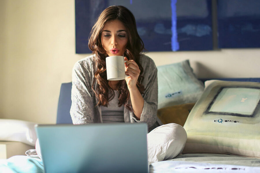 A woman drinking a cup of coffee on her bed looking up furnace replacement in London on her laptop