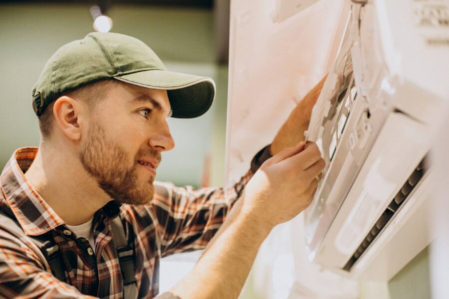 A man in a green cap fixing an AC unit for a blog post titled "Why is My Air Conditioner Leaking Water?"
